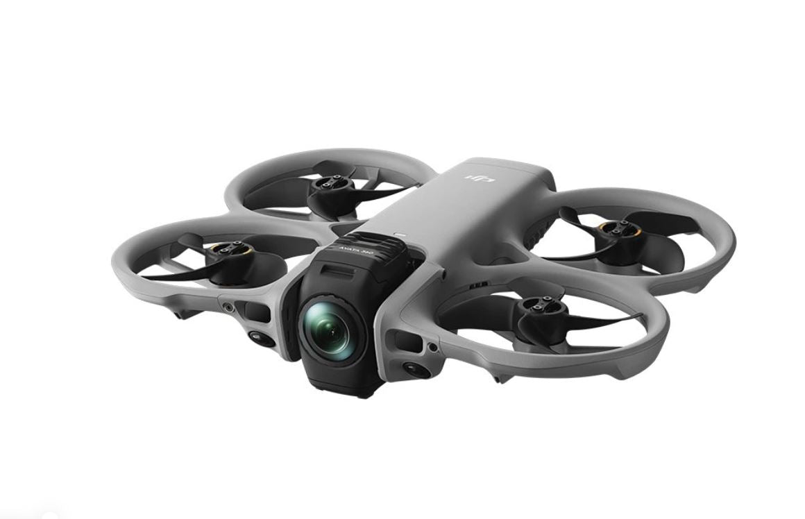 Dron FPV cu patru elice și cameră, carcasă gri, aspect compact.