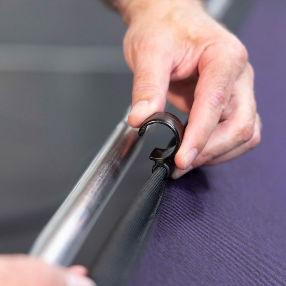 Mâna fixează panoul textil aubergine de cadrul metalic cu clemă