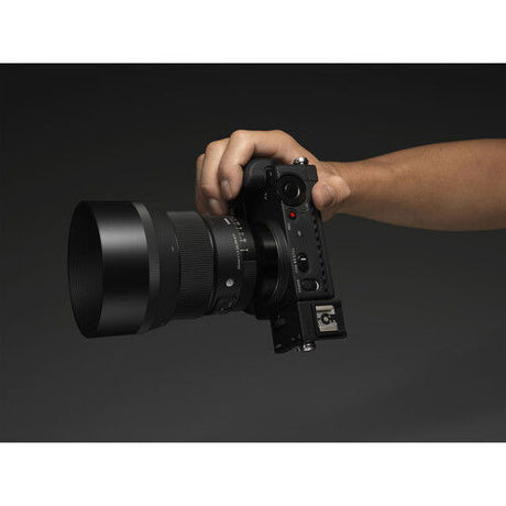 Person holding black 85mm f/1.4 DG DN Art lens mounted on camera