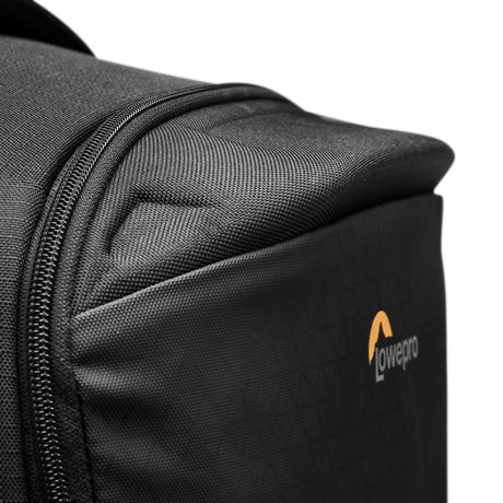 Close-up of gray backpack fabric, front corner seam, and orange logo patch