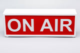 ON AIR illuminated sign with white casing, red face, and bold white “ON AIR” letters.