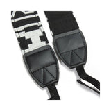 Close-up of camera strap ends: black leather pads with geometric black/white pattern