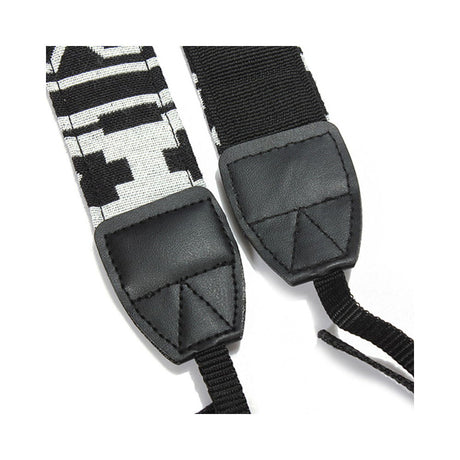 Close-up of camera strap ends: black leather pads with geometric black/white pattern