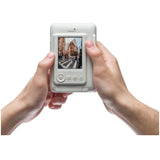 Misty white Instax mini LiPlay instant camera held in hands, LCD shows photo