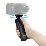 Hand holding black wireless shooting grip with photo/movie controls visible