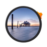 Circular ND filter showing a scene through tinted glass; orange pull tab visible