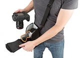 Black camera bag worn crossbody; hand opens access to padded lens compartments