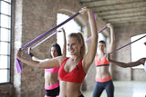 Resistance-band workout in gym with women holding purple bands overhead