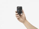 18-50mm f/2.8 DC DN zoom lens held in hand, front element and hood visible