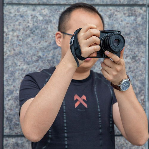 Person using black camera hand strap to steady a compact camera
