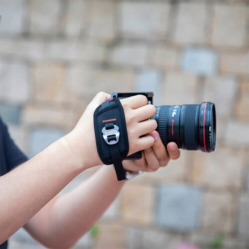 Hand holding camera with black wrist strap around the fingers and palm