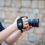 Hand holding camera with black wrist strap around the fingers and palm
