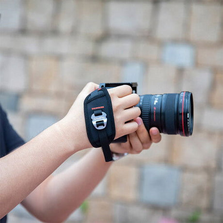 Hand holding camera with black wrist strap around the fingers and palm