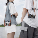 Brown leather camera strap worn crossbody with metal ring ends