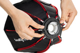 Hands fitting the front diffuser ring on a black and red RA-D30 mini softbox