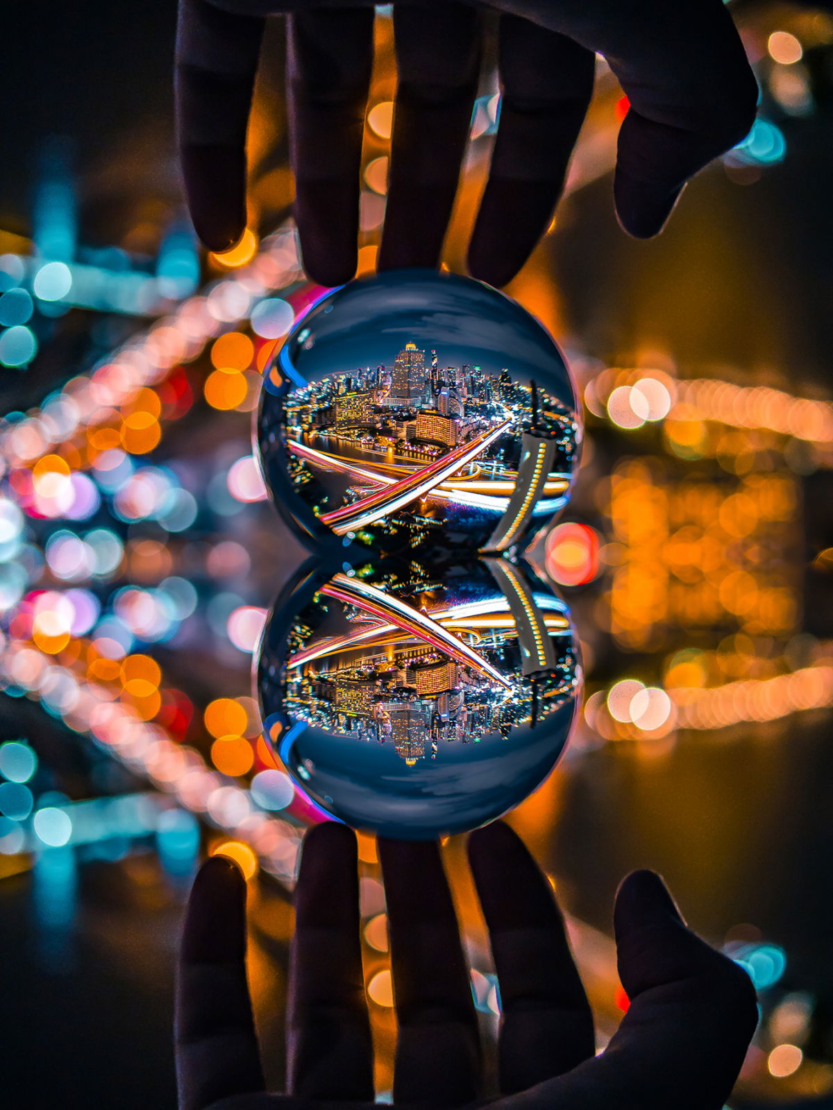 Two clear glass spheres held in hands, reflecting colorful city lights