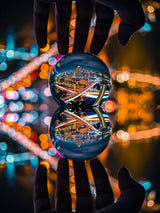 Two clear glass spheres held in hands, reflecting colorful city lights