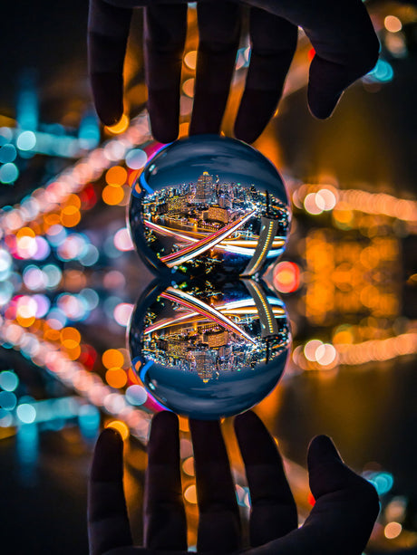 Two clear glass spheres held in hands, reflecting colorful city lights